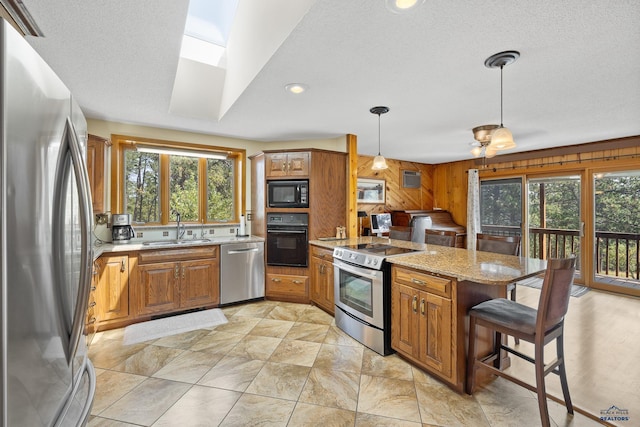 kitchen featuring sink, a breakfast bar area, light stone counters, pendant lighting, and black appliances