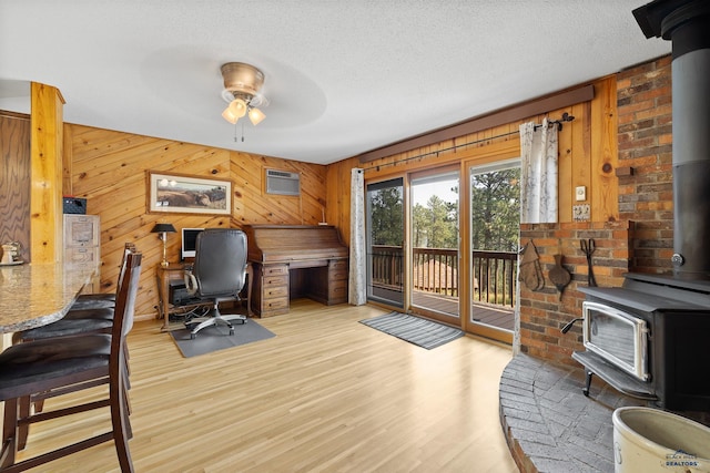 home office with an AC wall unit, a wood stove, a textured ceiling, and light hardwood / wood-style flooring