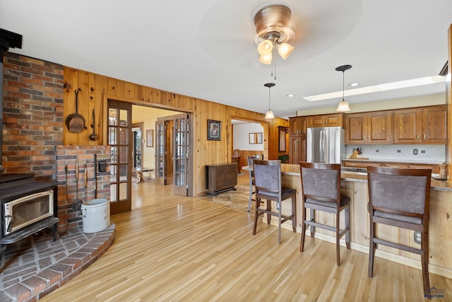 kitchen with a wood stove, stainless steel refrigerator, hanging light fixtures, light hardwood / wood-style floors, and wood walls