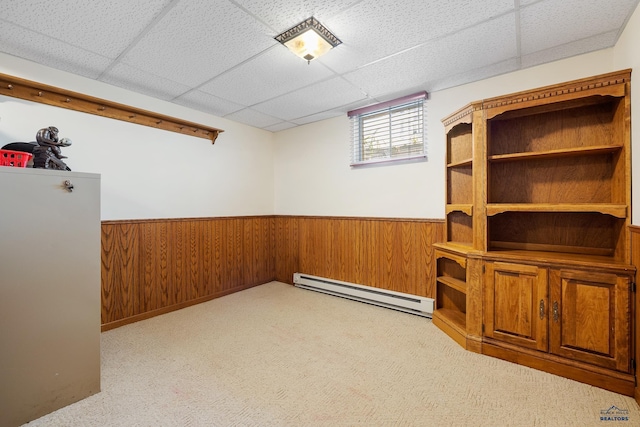 interior space with light colored carpet, wooden walls, a drop ceiling, and a baseboard heating unit