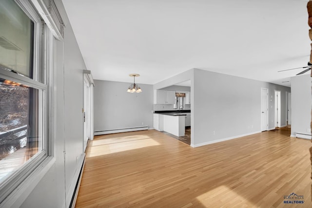 unfurnished living room with a baseboard heating unit, ceiling fan with notable chandelier, and light wood-type flooring