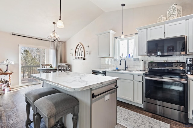 kitchen featuring lofted ceiling, appliances with stainless steel finishes, hanging light fixtures, a center island, and white cabinets