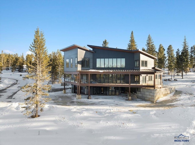 snow covered rear of property featuring a sunroom