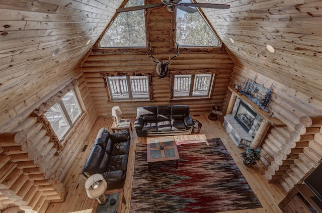 unfurnished living room with a stone fireplace, ceiling fan, high vaulted ceiling, wood-type flooring, and log walls
