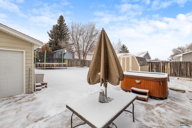 snow covered patio featuring a hot tub, a trampoline, and a storage unit