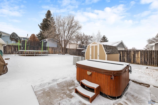 snowy yard featuring a hot tub, a trampoline, and a storage unit