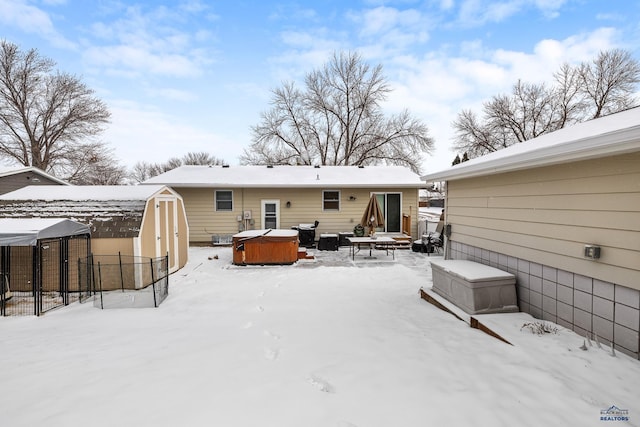 snow covered back of property featuring a hot tub and a storage shed