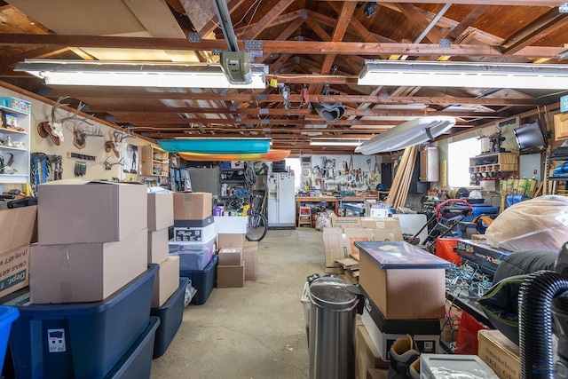 garage featuring a garage door opener, white refrigerator with ice dispenser, and a workshop area