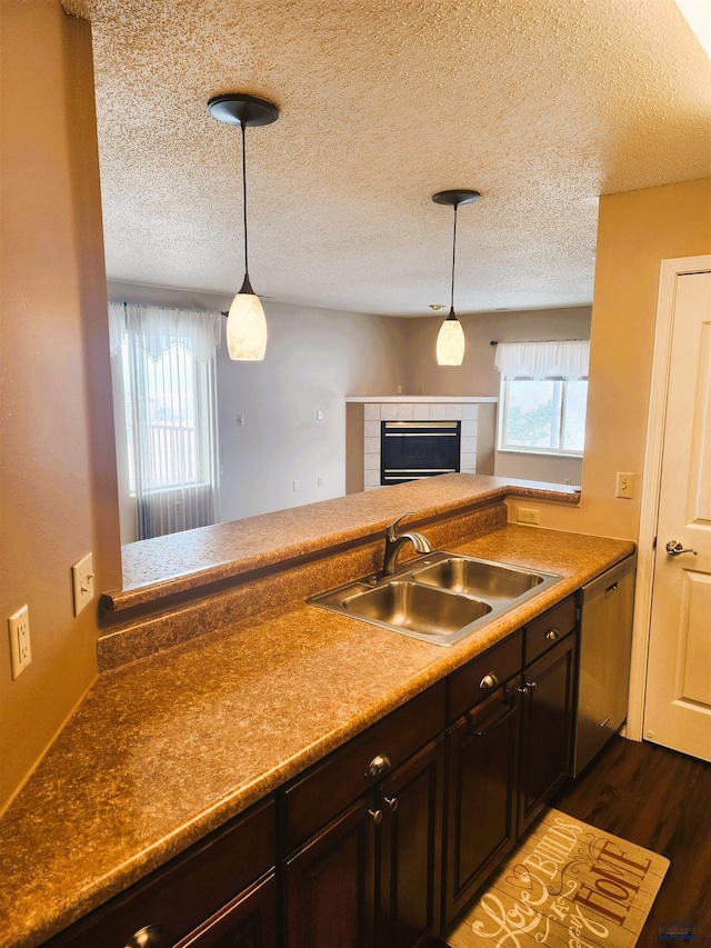 kitchen with sink, stainless steel dishwasher, a tile fireplace, a wealth of natural light, and pendant lighting