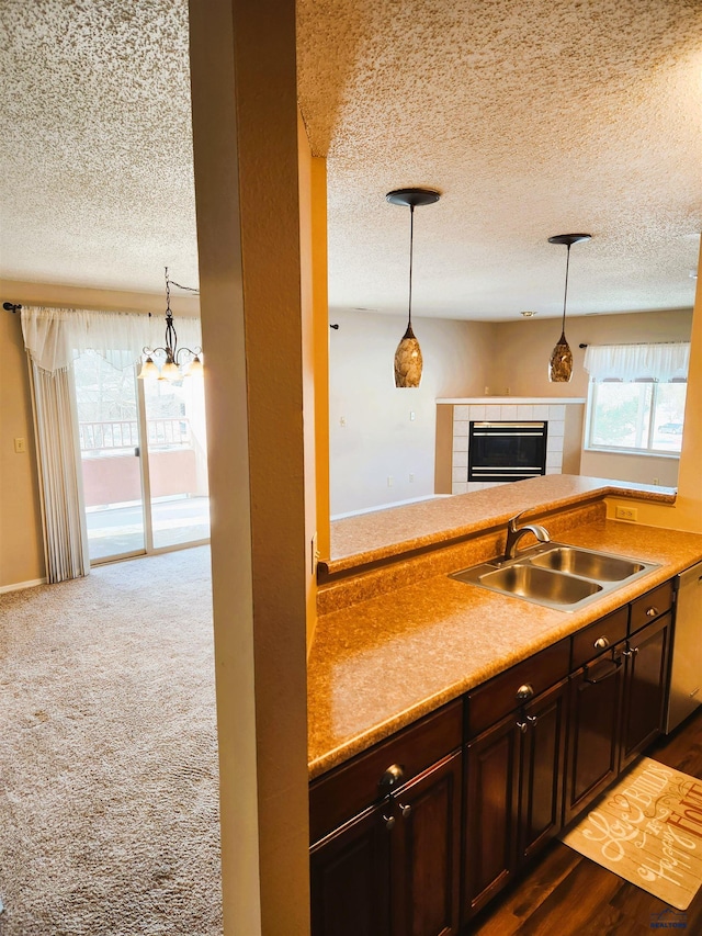 kitchen featuring sink, dishwasher, dark brown cabinets, dark colored carpet, and a tiled fireplace