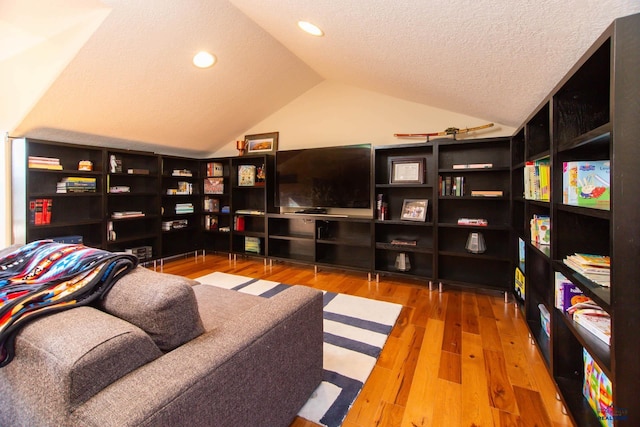 living area with lofted ceiling, wood-type flooring, and a textured ceiling