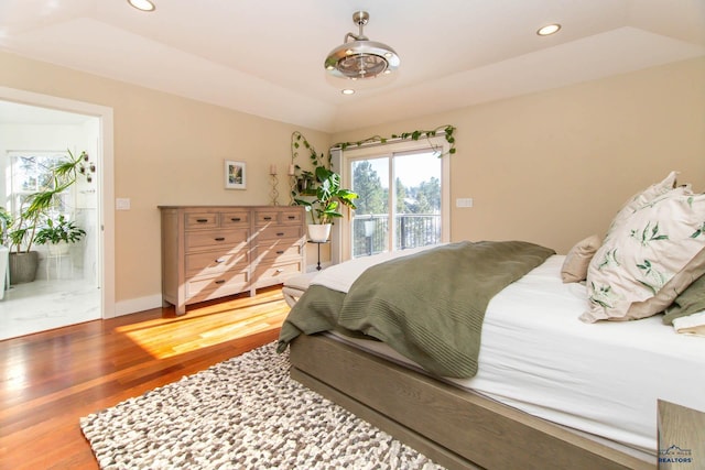 bedroom with access to exterior, a tray ceiling, wood-type flooring, and vaulted ceiling