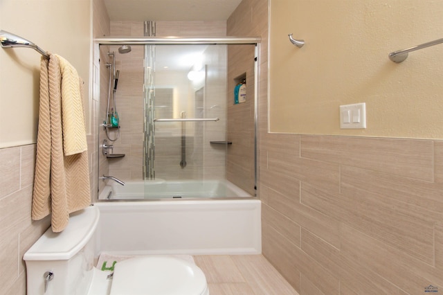 bathroom with toilet, combined bath / shower with glass door, and tile walls