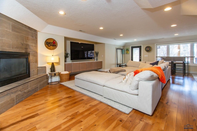 living room with hardwood / wood-style flooring, a tile fireplace, and a textured ceiling