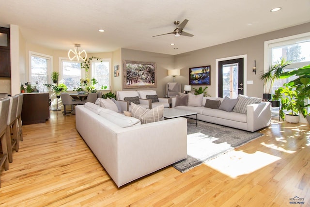 living room with ceiling fan with notable chandelier, light hardwood / wood-style flooring, and a healthy amount of sunlight