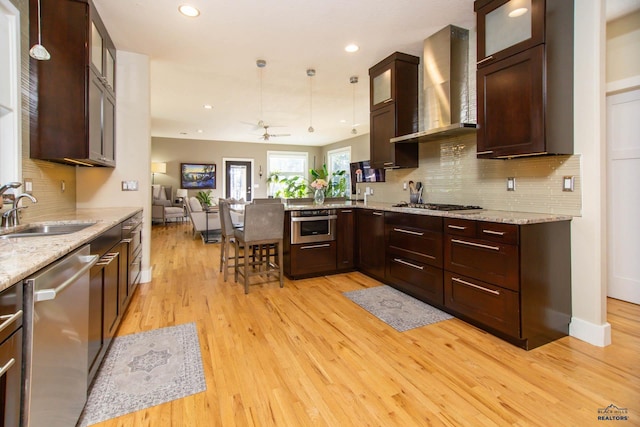 kitchen featuring pendant lighting, sink, stainless steel appliances, light stone countertops, and wall chimney exhaust hood