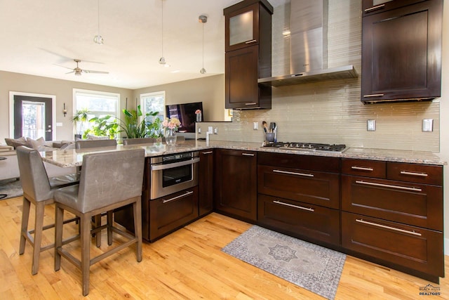 kitchen featuring light stone countertops, wall chimney exhaust hood, kitchen peninsula, and a breakfast bar area