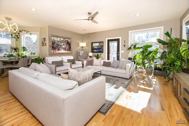 living room with ceiling fan with notable chandelier and light hardwood / wood-style floors