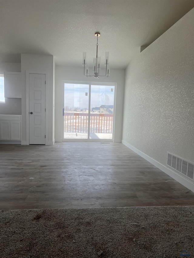 unfurnished dining area with an inviting chandelier, dark wood-type flooring, and a textured ceiling