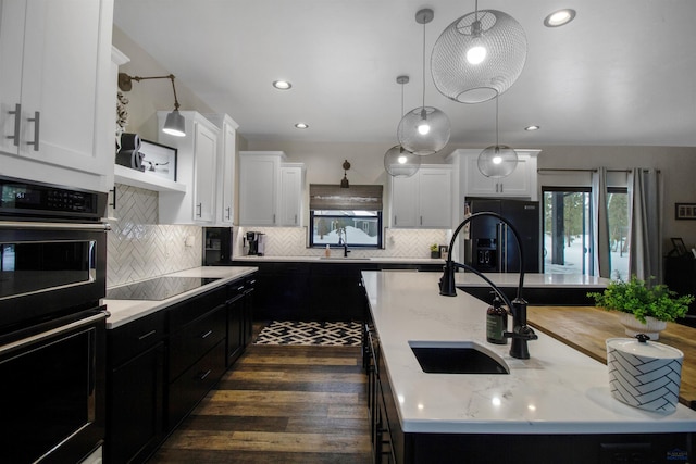 kitchen featuring an island with sink, pendant lighting, white cabinets, and black appliances