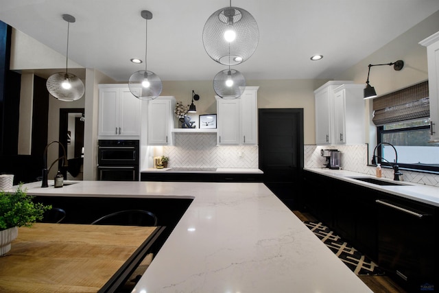 kitchen featuring sink, a breakfast bar area, white cabinetry, hanging light fixtures, and black appliances