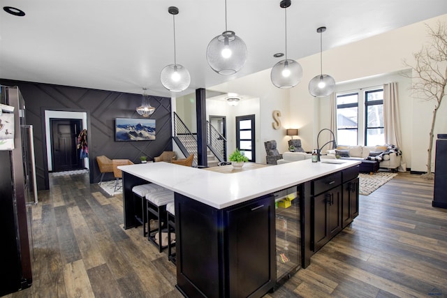 kitchen featuring sink, decorative light fixtures, dark hardwood / wood-style flooring, beverage cooler, and a kitchen island with sink