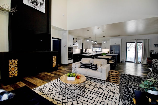 living room featuring sink, a towering ceiling, and dark wood-type flooring