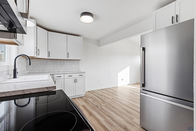 kitchen featuring stainless steel refrigerator, white cabinetry, sink, decorative backsplash, and light wood-type flooring