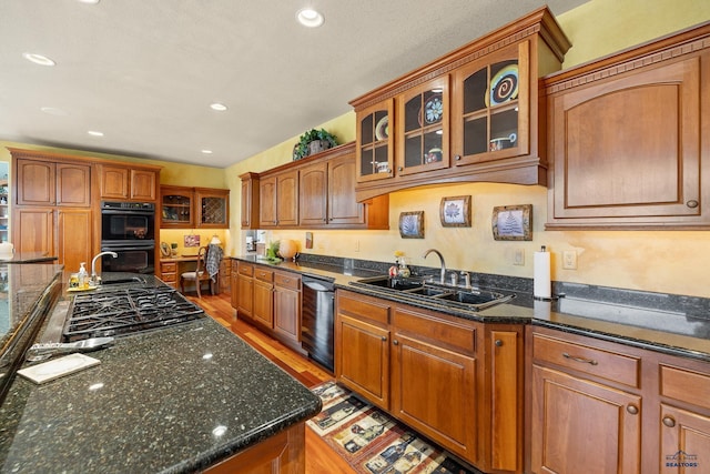 kitchen featuring dark stone countertops, sink, light hardwood / wood-style flooring, and black appliances