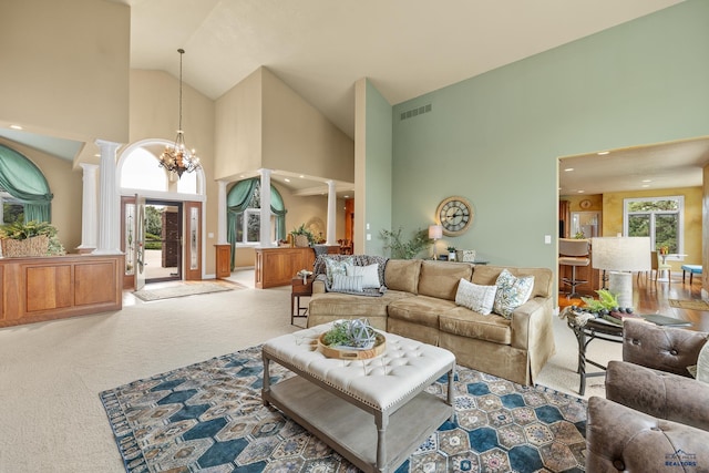 carpeted living room featuring high vaulted ceiling, decorative columns, and a chandelier