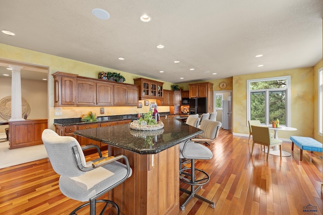 kitchen with a kitchen island, decorative columns, a kitchen bar, light hardwood / wood-style floors, and black refrigerator with ice dispenser