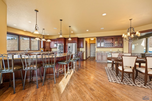 kitchen with appliances with stainless steel finishes, hanging light fixtures, a breakfast bar area, and light hardwood / wood-style flooring