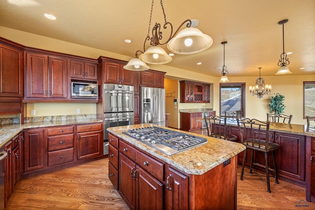 kitchen featuring hanging light fixtures, stainless steel appliances, a center island, light stone counters, and light hardwood / wood-style floors