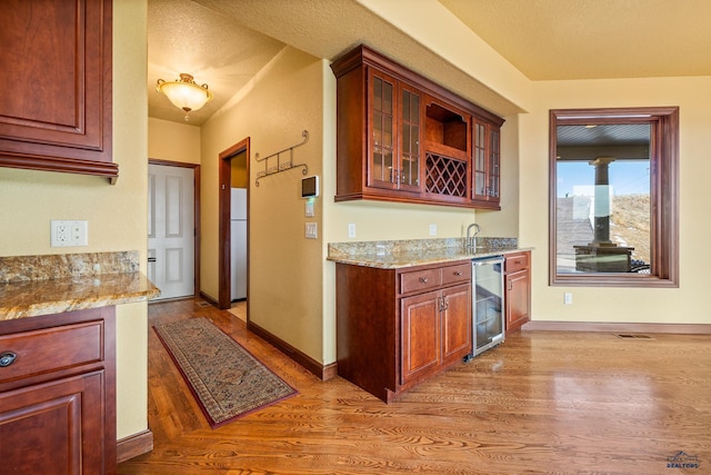 kitchen with sink, wood-type flooring, fridge, beverage cooler, and light stone countertops