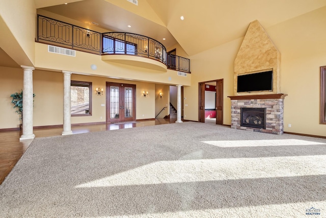 unfurnished living room featuring french doors, carpet flooring, high vaulted ceiling, and ornate columns