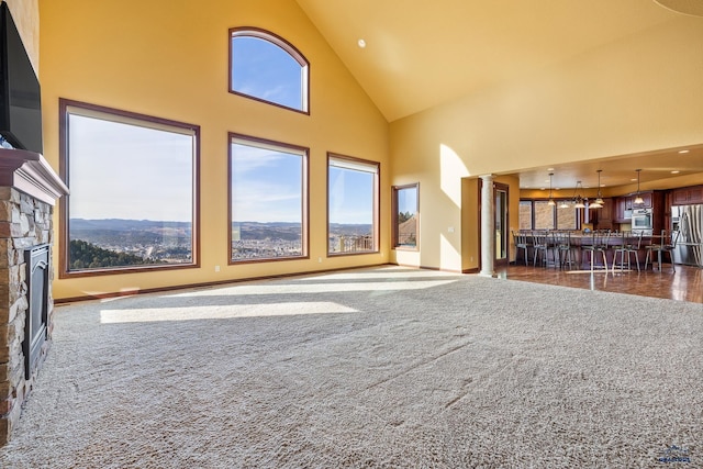 unfurnished living room with high vaulted ceiling, dark carpet, a wealth of natural light, and decorative columns