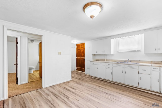 kitchen with light wood-type flooring, sink, white cabinets, and a textured ceiling