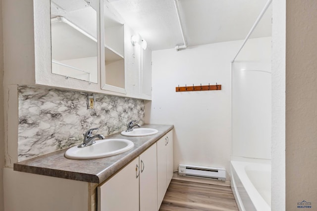 bathroom featuring bathing tub / shower combination, wood-type flooring, decorative backsplash, vanity, and a baseboard heating unit