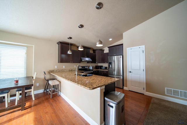 kitchen featuring stainless steel appliances, decorative light fixtures, vaulted ceiling, sink, and kitchen peninsula