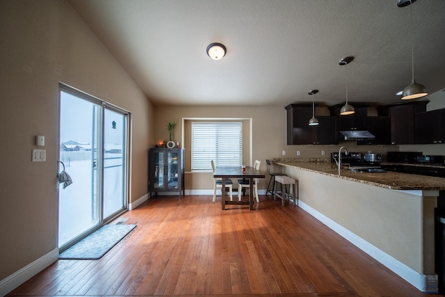 kitchen with dark stone counters, decorative light fixtures, light hardwood / wood-style floors, range with electric stovetop, and kitchen peninsula