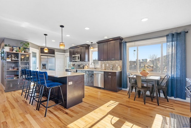 kitchen featuring stainless steel appliances, light countertops, dark brown cabinetry, and decorative light fixtures