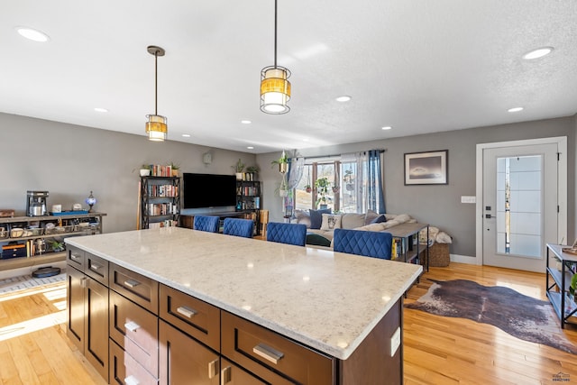 kitchen featuring light stone counters, a kitchen island, open floor plan, light wood finished floors, and pendant lighting