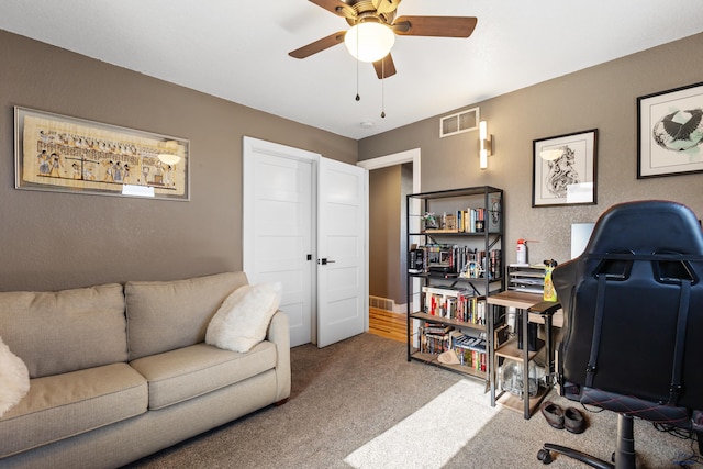 office area with a textured wall, carpet floors, visible vents, and a ceiling fan