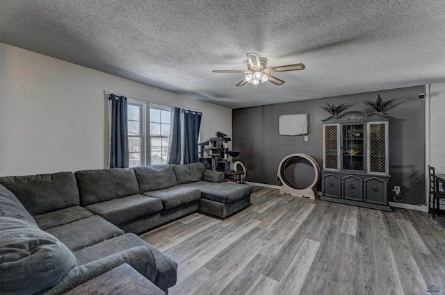 living room featuring ceiling fan, a textured ceiling, baseboards, and wood finished floors