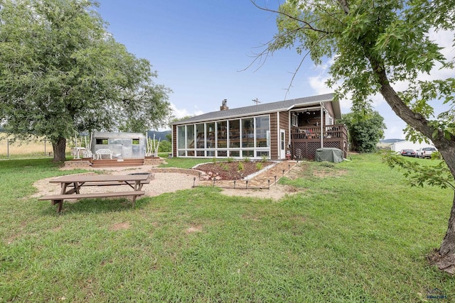 rear view of house featuring a yard, a chimney, a wooden deck, and a sunroom