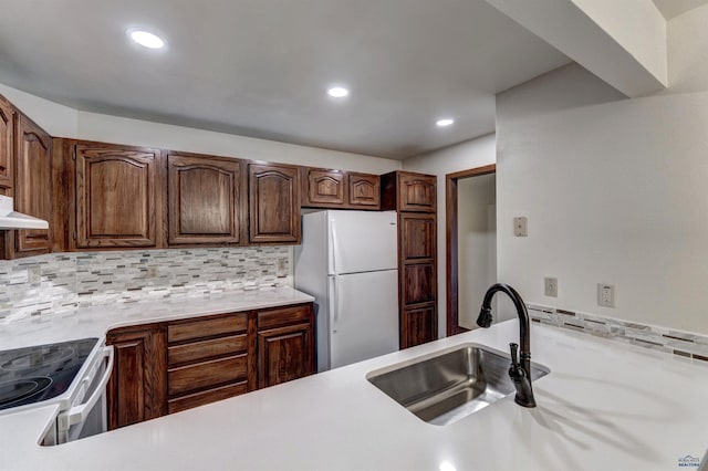 kitchen with under cabinet range hood, white appliances, a sink, light countertops, and tasteful backsplash