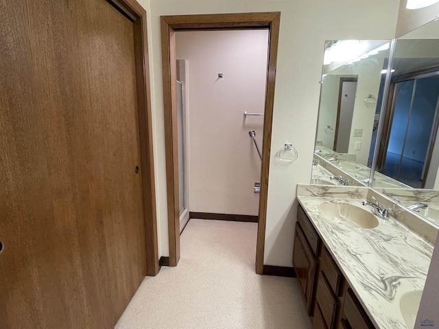 full bath featuring double vanity, baseboards, a sink, and a shower with shower door