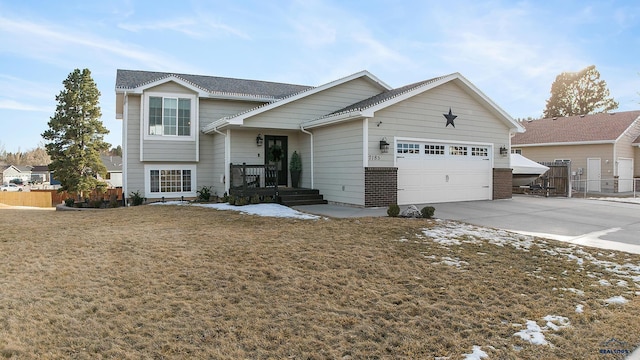 split level home with driveway, a garage, fence, a front yard, and brick siding