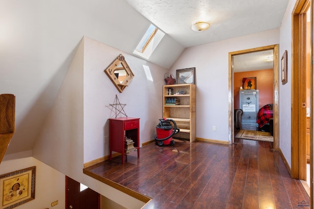 additional living space with vaulted ceiling with skylight, baseboards, dark wood finished floors, and a textured ceiling