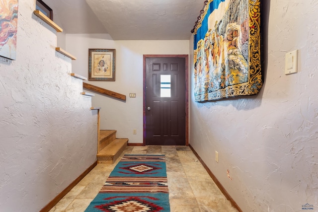 doorway featuring a textured ceiling, a textured wall, stairway, and baseboards